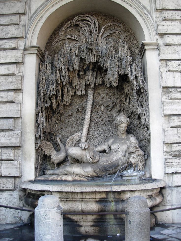 a statue is shown in front of a building with palm trees on the wall and water running through it