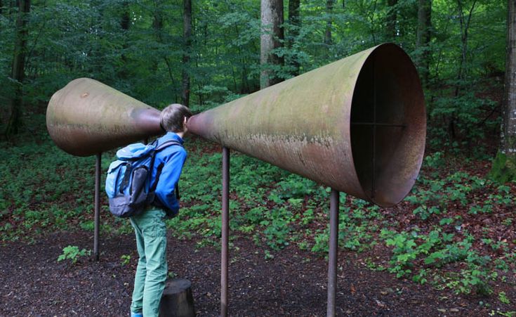 a person with a backpack is looking through two large metal objects in the woods,