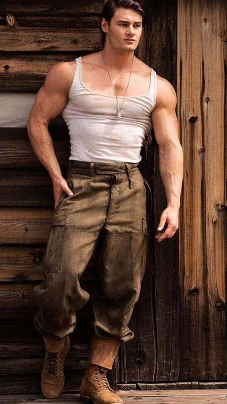 a man standing in front of a wooden wall wearing brown pants and a white tank top