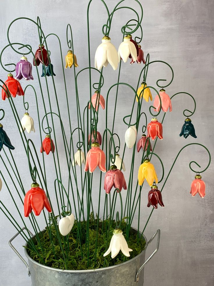 a metal bucket filled with lots of flowers on top of a grass covered floor next to a wall