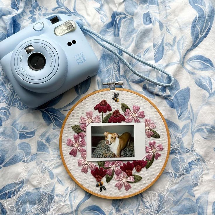 a camera and some flowers on a bed with a blue case next to the photo