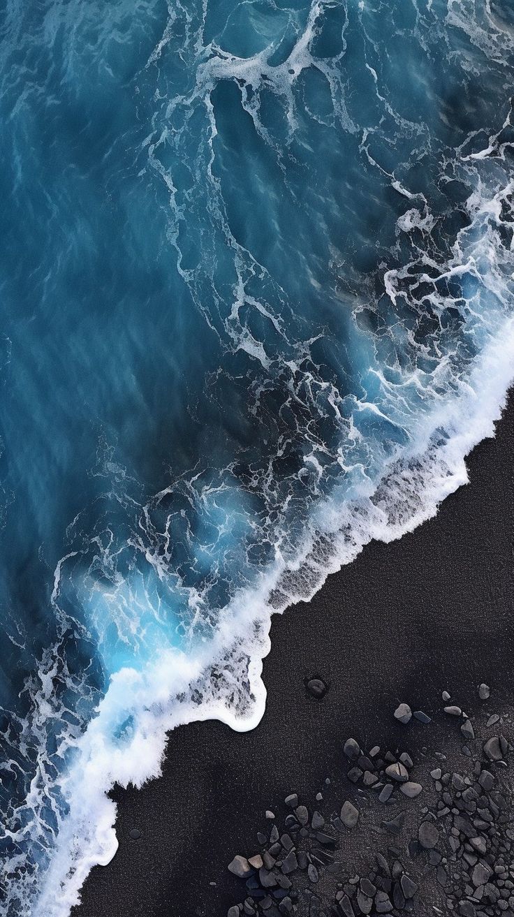 an aerial view of the ocean waves and black sand beach