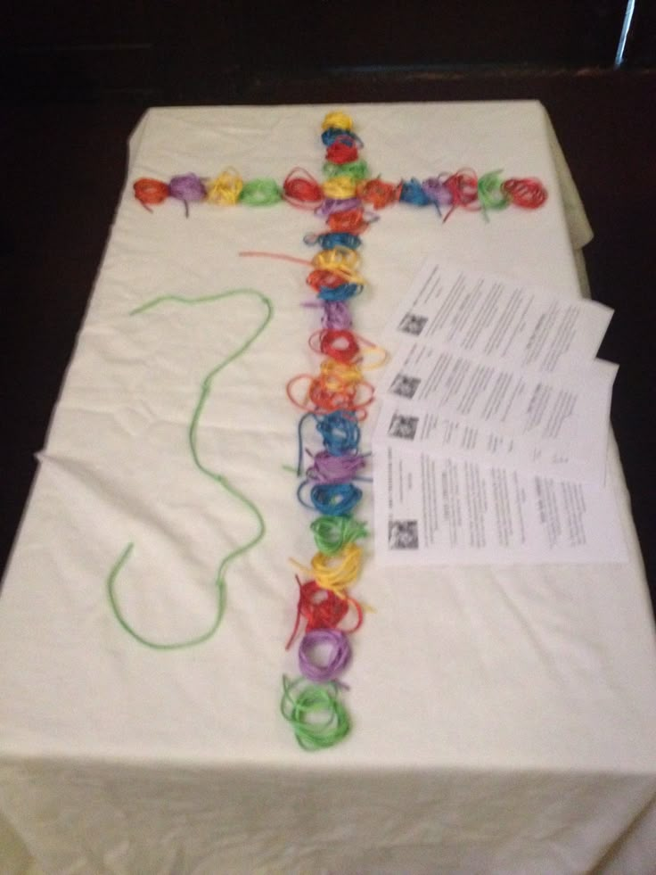 a cross made out of plastic beads sitting on top of a white tablecloth covered box