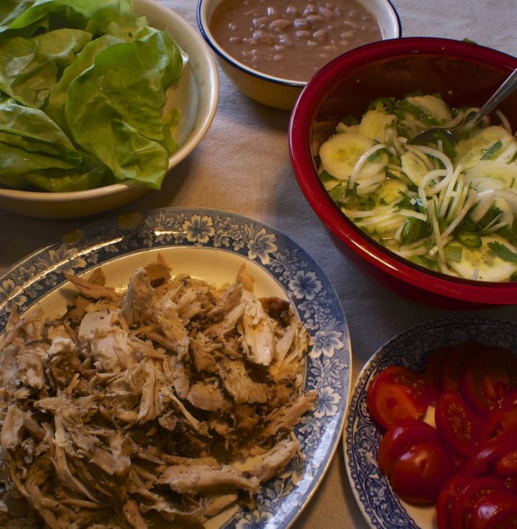 a table topped with plates of food and bowls of salad next to tortillas