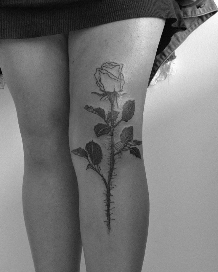 a black and white photo of a woman's thigh with a rose tattoo