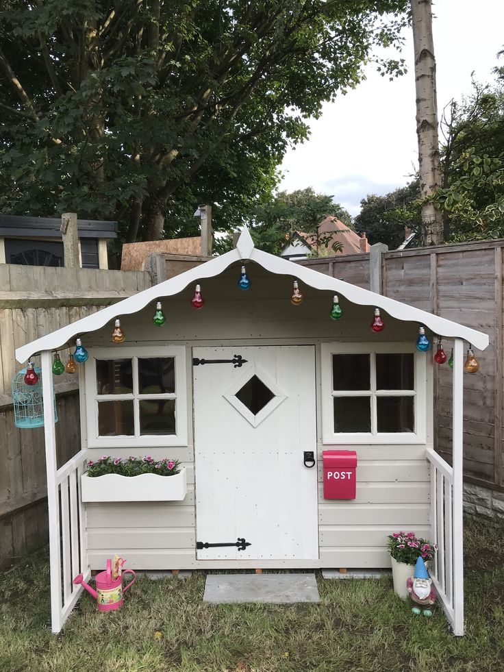 a small white shed sitting in the middle of a yard with christmas decorations on it