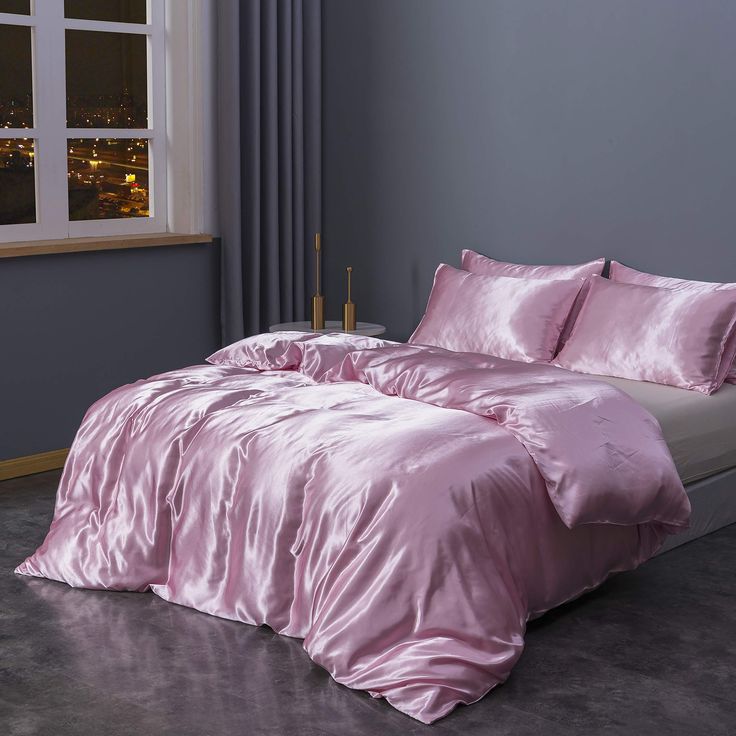 a bed with pink comforter and pillows in a room next to a large window