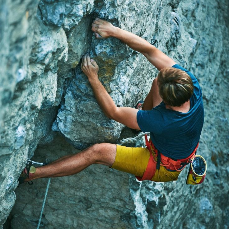 a man climbing up the side of a mountain with his hands on his hips while holding onto a rope