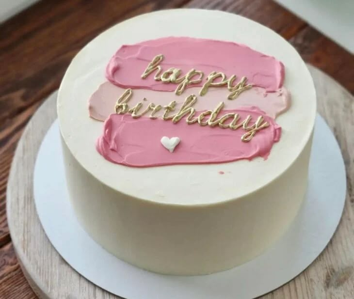 a white cake with pink frosting and gold lettering on it that says happy birthday