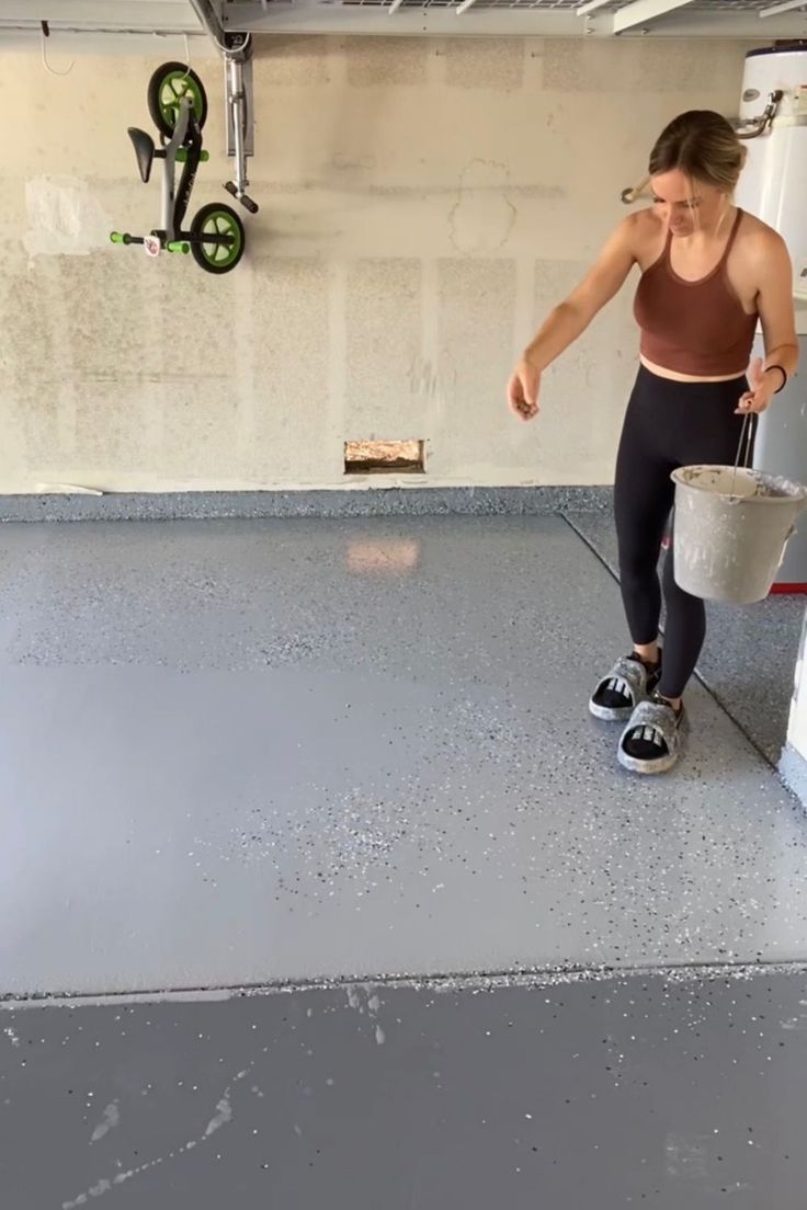 a woman is standing in the garage holding a bucket