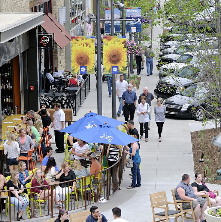 many people are sitting at tables outside on the sidewalk with sunflowers in the background