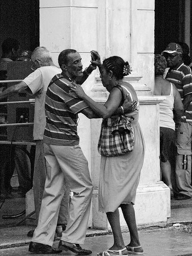 a man and woman standing next to each other in front of a building with people looking on