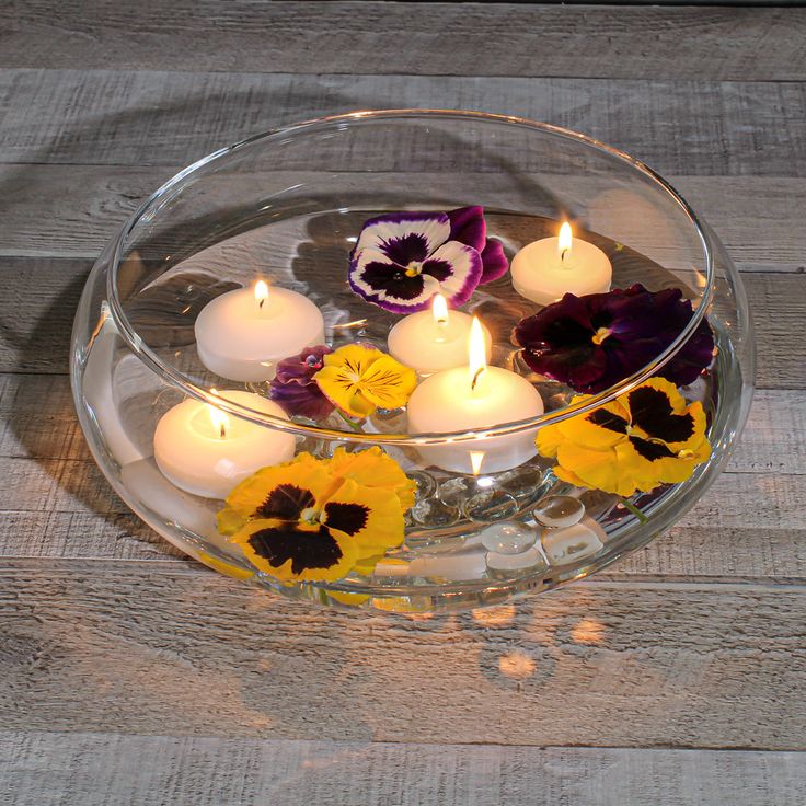 a glass bowl filled with flowers and lit candles