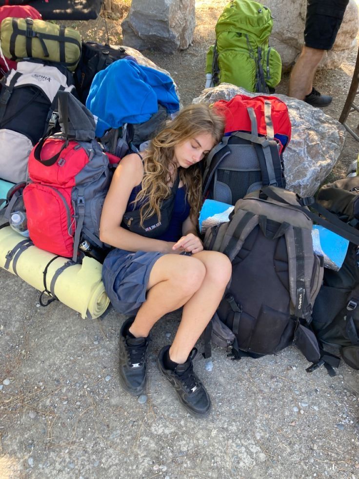 a young woman sitting on the ground surrounded by backpacks