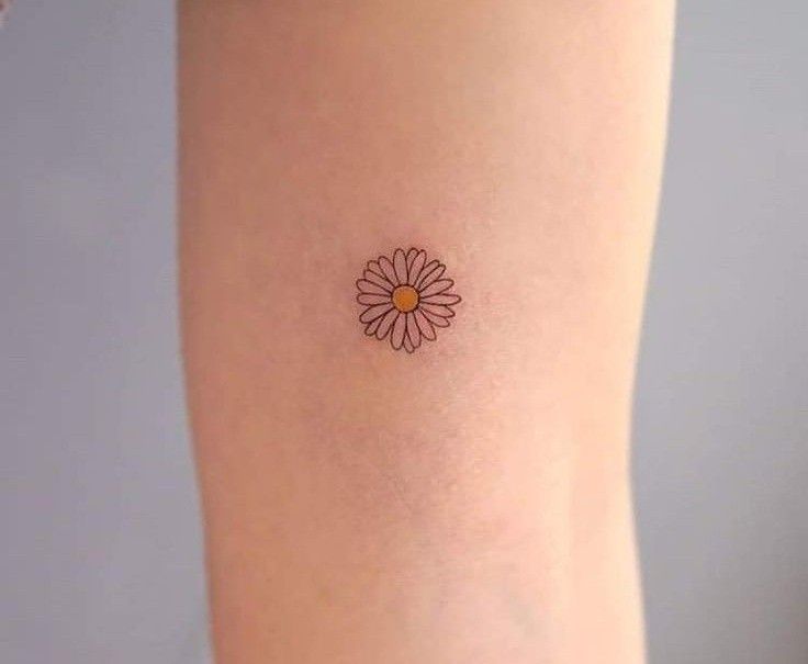 a small daisy tattoo on the right arm, with an orange dot in the center