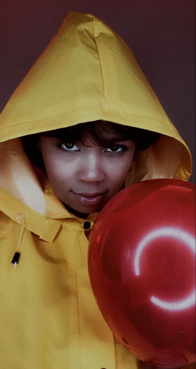 a woman wearing a yellow raincoat and holding a red ball in her hand with the hood up