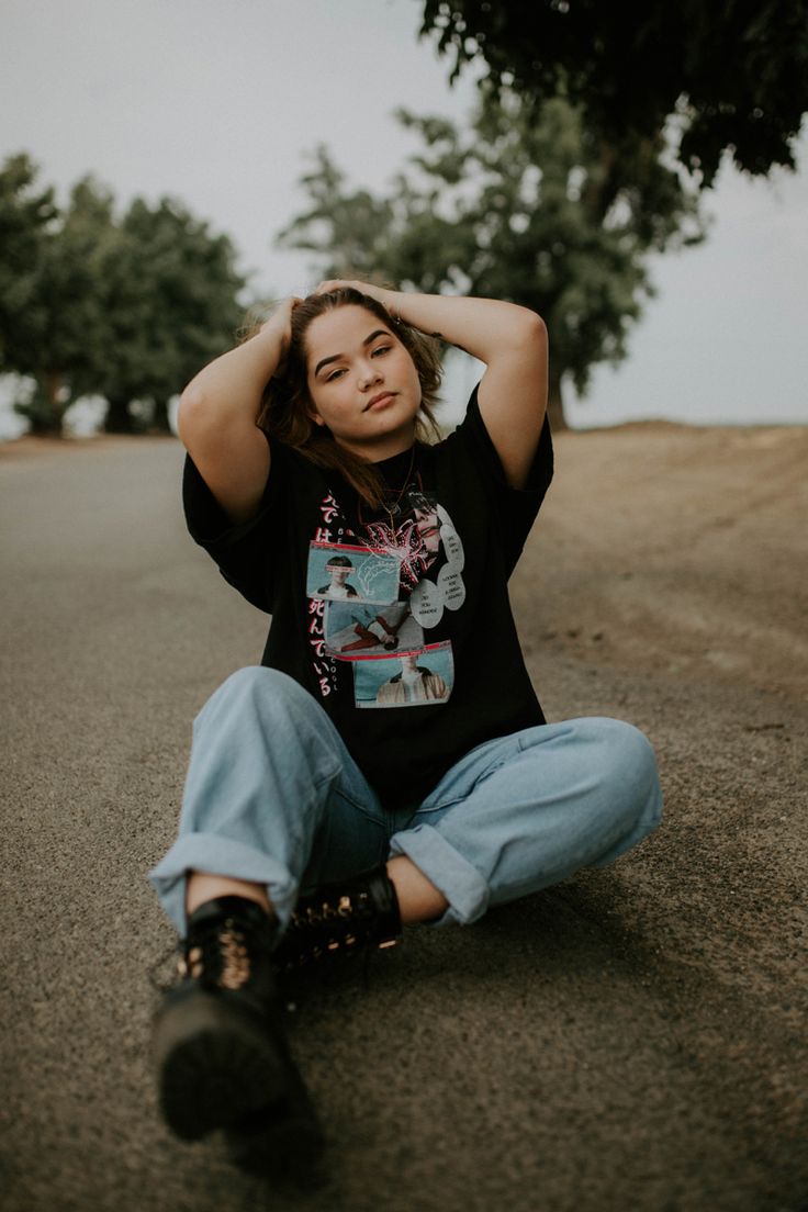 a young woman sitting on the ground with her hands behind her head and looking at the camera