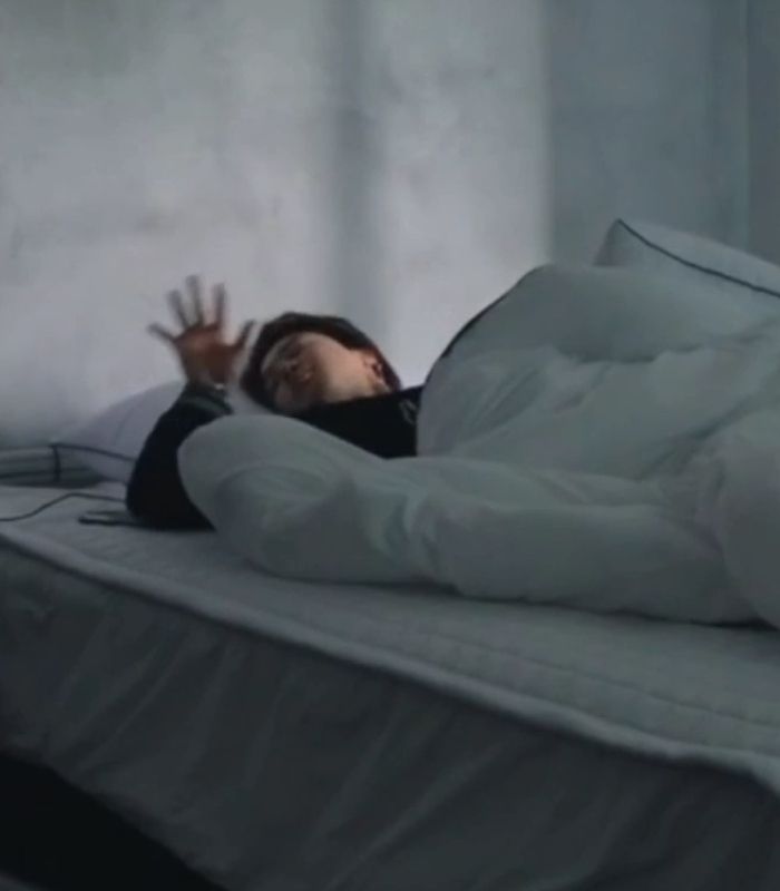 a woman laying on top of a bed with her hands up in the air as if to fall asleep