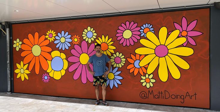 a man standing in front of a large flowered wall with flowers painted on it