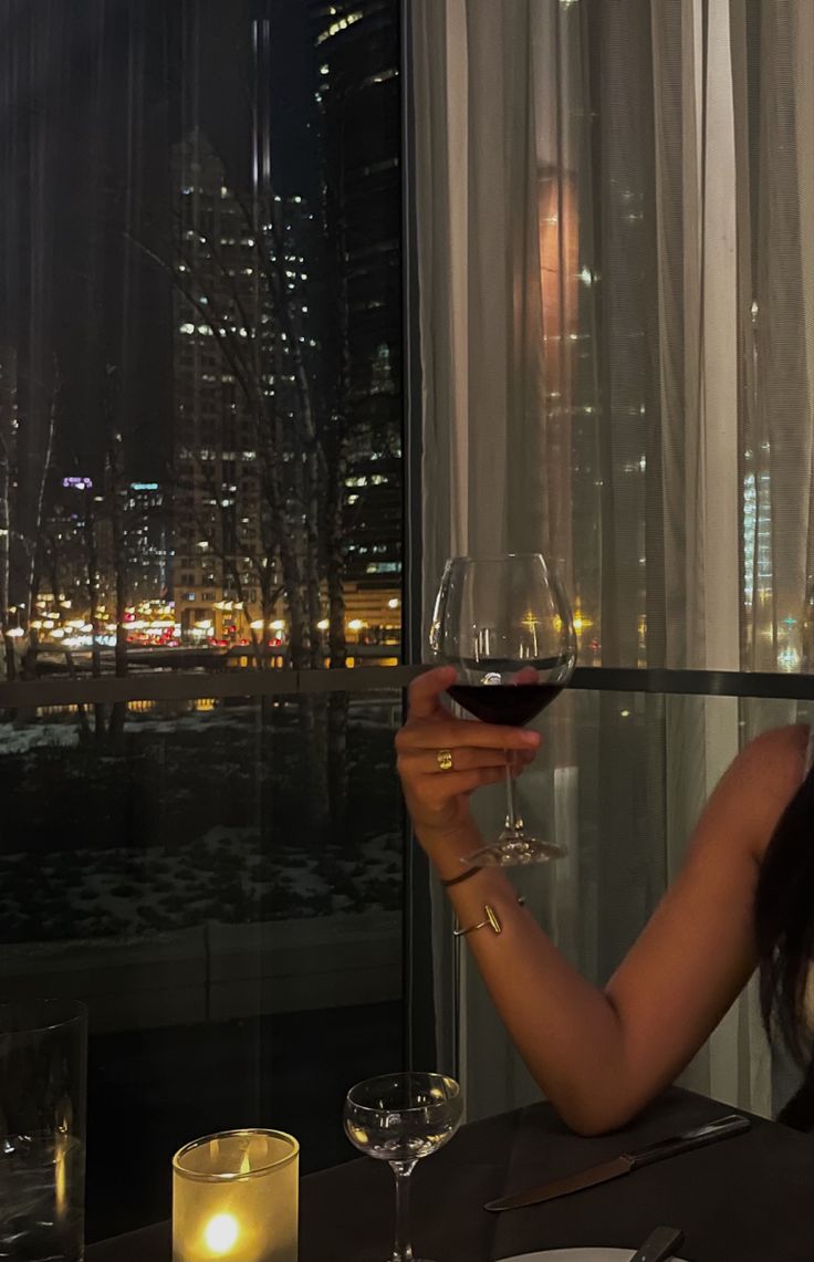 a woman sitting at a table with a glass of wine in front of the window