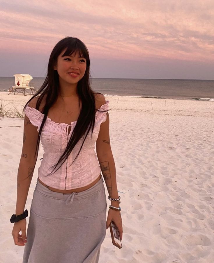 a woman standing on top of a sandy beach next to the ocean with a pink sky in the background