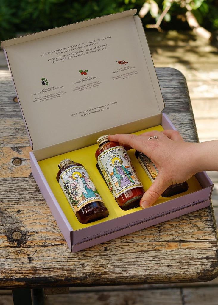 a person is holding onto two bottles of sauce in a box on a wooden table