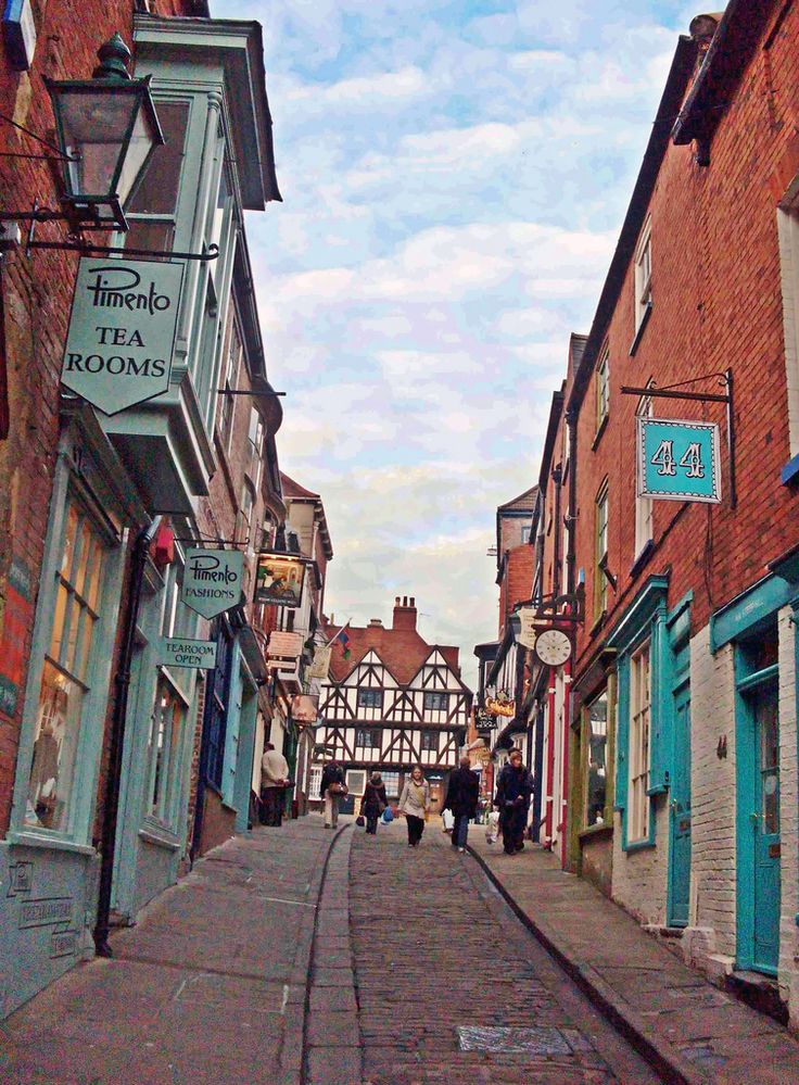 people walking down an alleyway between two buildings with shops on each side and one building that has a sign for tea rooms