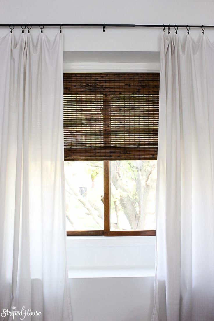 an open window with white curtains and bamboo blinds