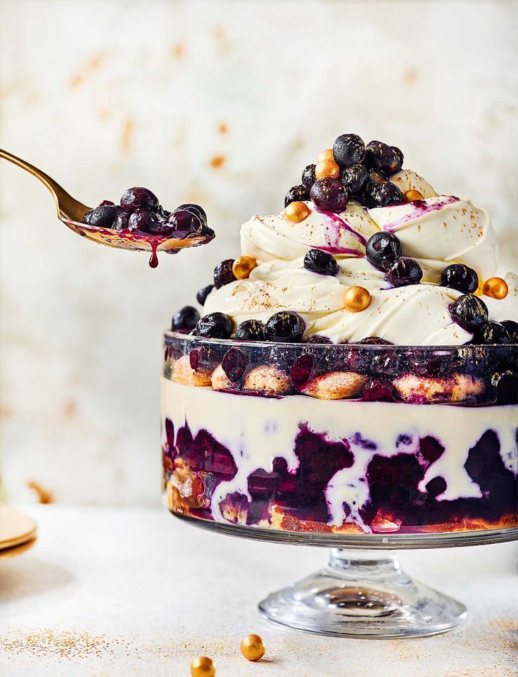 a blueberry trifle with whipped cream and berries on top is being lifted by a spoon