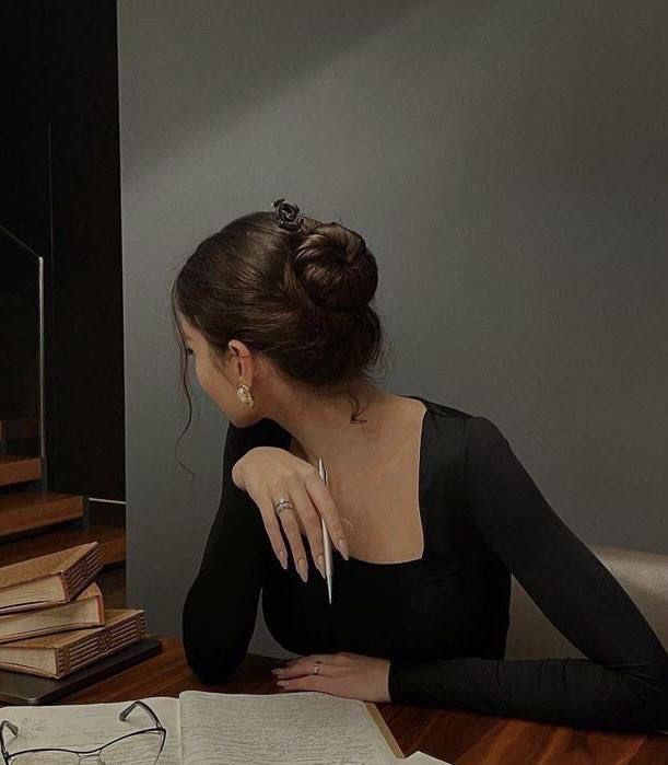 a woman sitting at a desk with an open book in front of her and reading glasses on the table