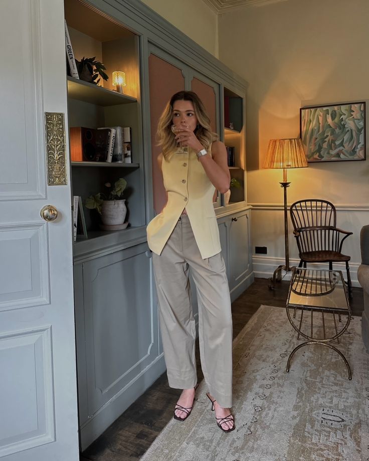 a woman is taking a selfie in her living room while wearing a yellow blazer and khaki pants