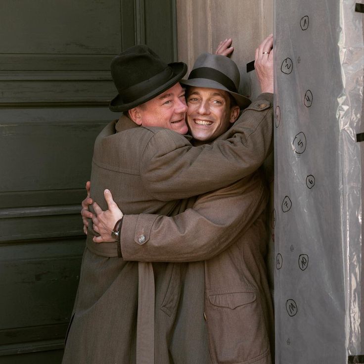 two older people hugging each other in front of a door with their arms around one another