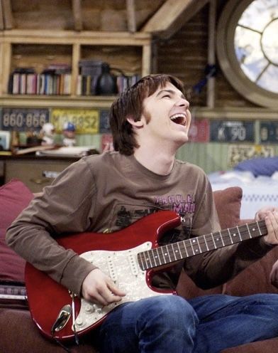 a young man is laughing while playing an electric guitar