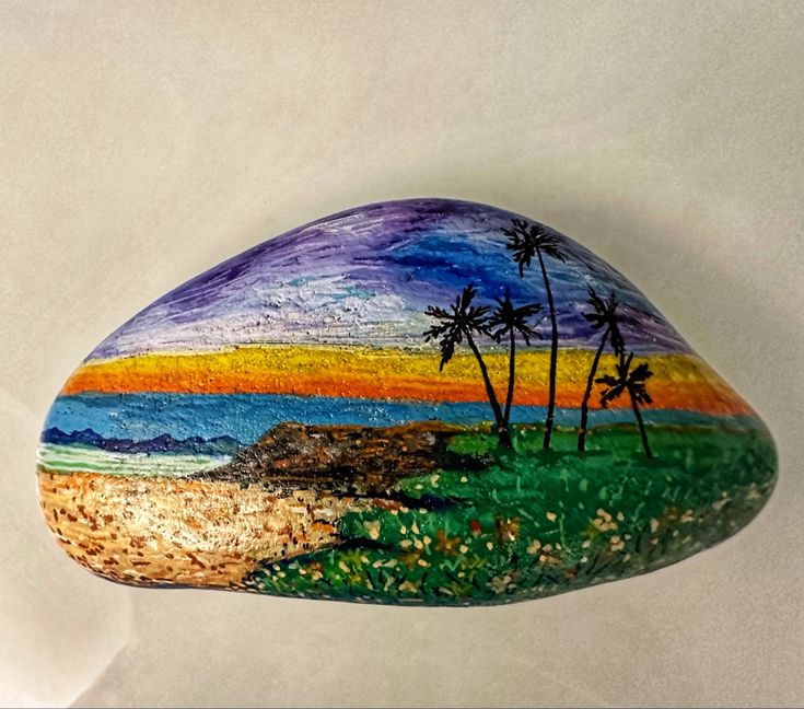 a painted rock sitting on top of a white table next to a painting of palm trees