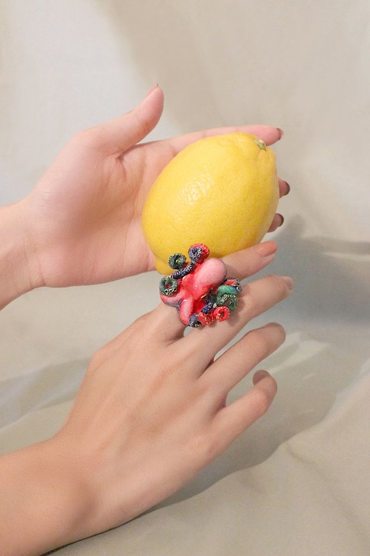 a woman's hand holding a yellow fruit with berries on it and an orange in the other hand