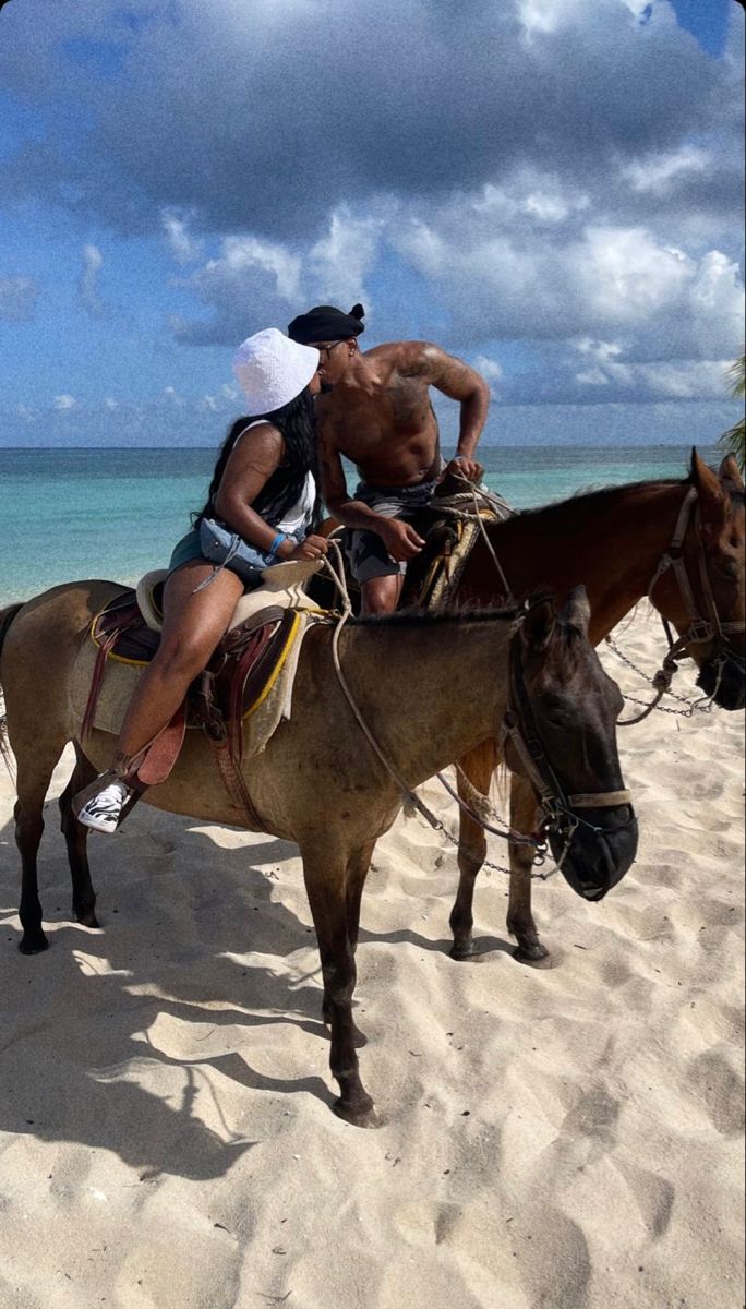 two people riding horses on the beach with water in the backgrouds and clouds in the sky