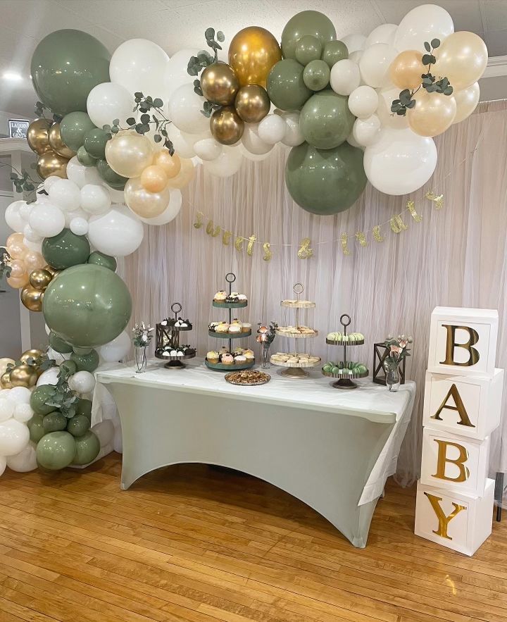 a table topped with lots of balloons next to a white and green cake stand on top of a hard wood floor