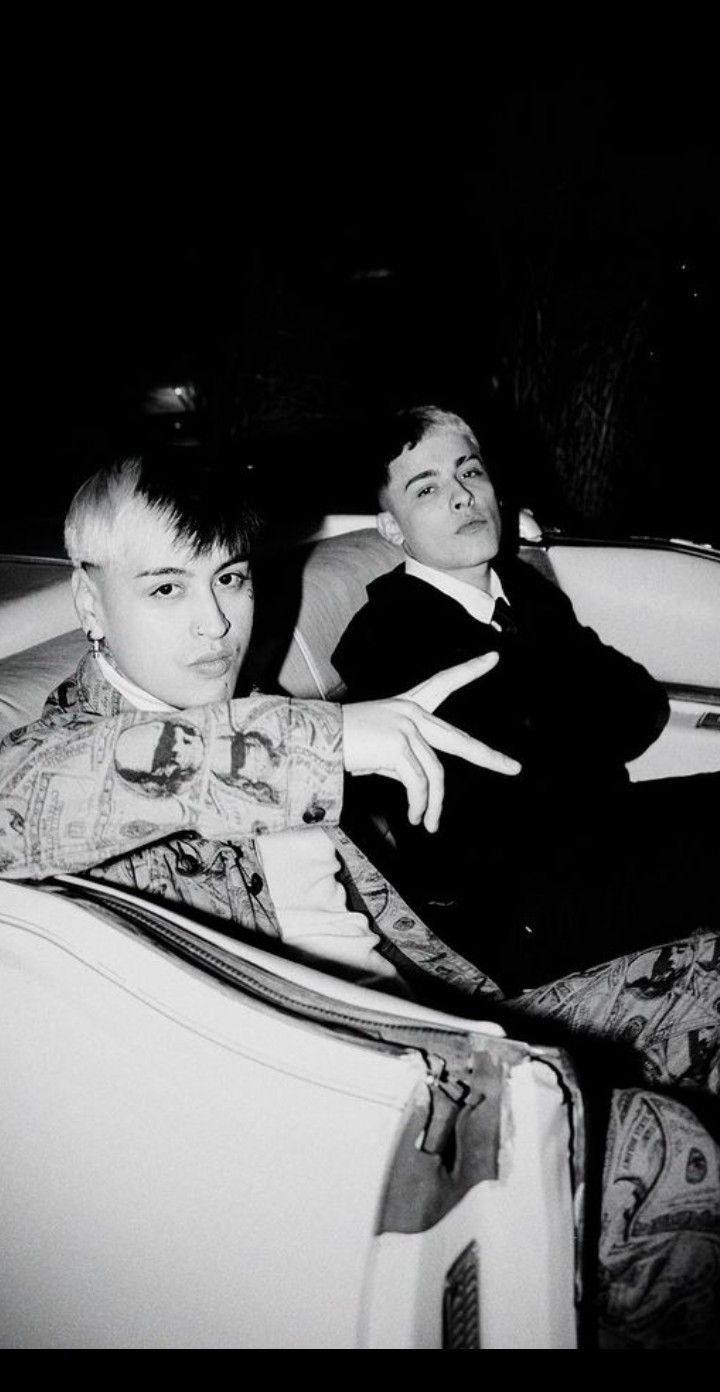 two young men sitting in the back of a convertible car at night, one pointing