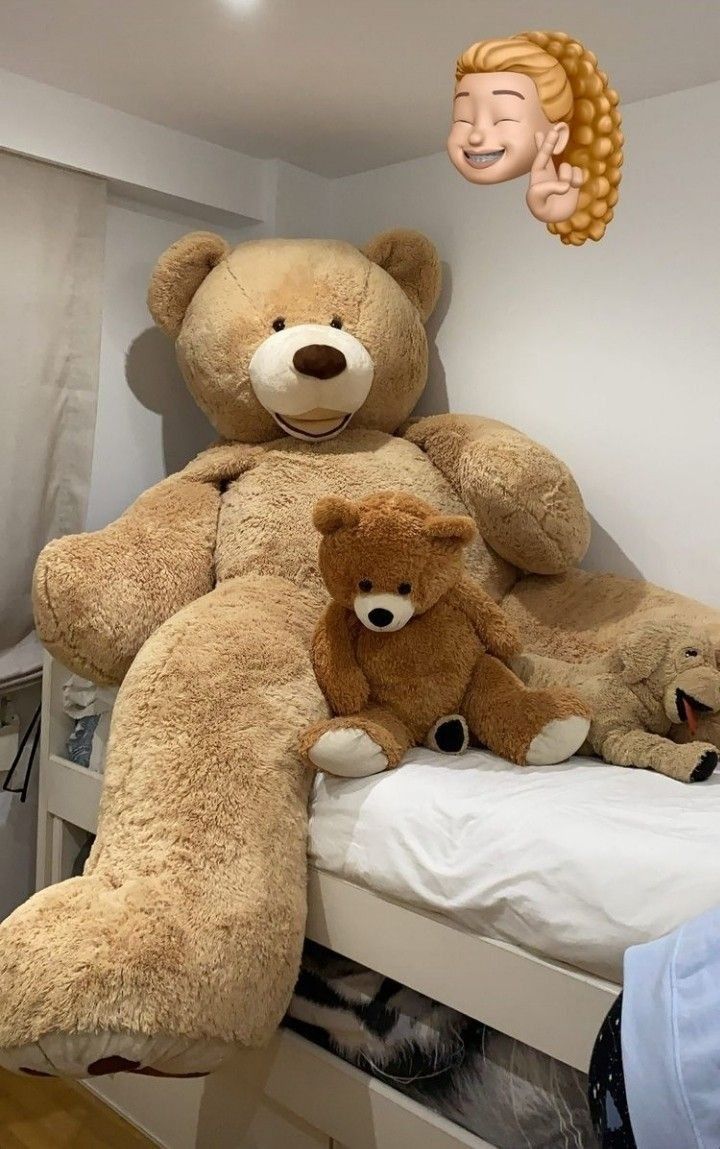 there is a large teddy bear sitting on the bed with two smaller stuffed animals in front of it