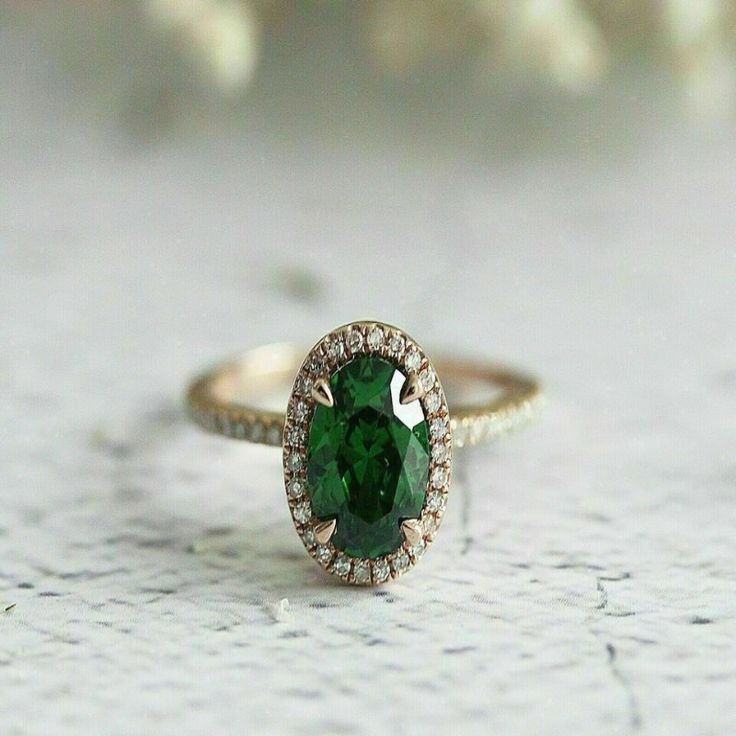 a close up of a ring with a green stone in the center and diamonds around it