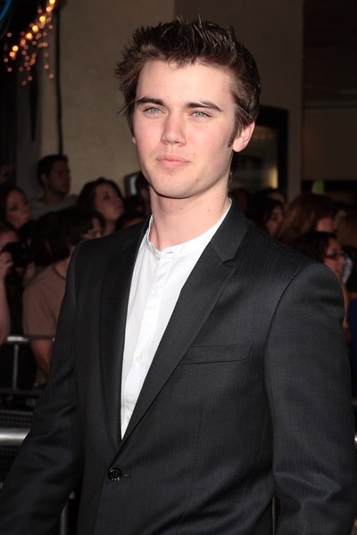 a young man in a black suit and white shirt standing next to a group of people