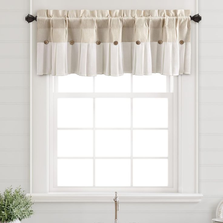 a kitchen window with white curtains and black hardware on the valance over the sink