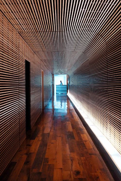 an empty hallway with wood flooring and wooden slats on the wall behind it