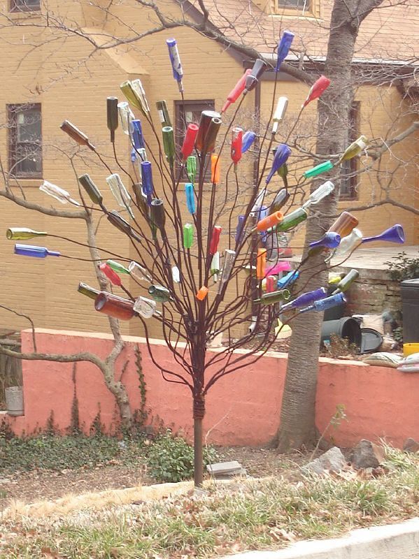 there is a tree made out of many different colored bottles in the grass next to a building