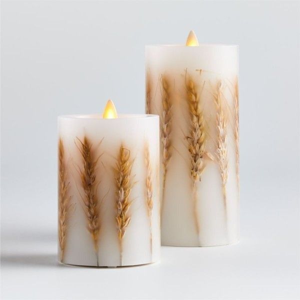 two candles with dried plants on them sitting next to each other in front of a white background