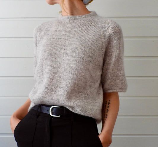 a woman wearing a gray sweater and black pants is standing in front of a white wall