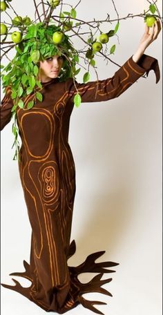 a woman dressed as a tree with branches and leaves on her head, standing in front of a white background