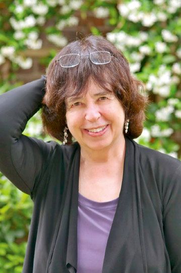 a woman with glasses is smiling for the camera while standing in front of some bushes