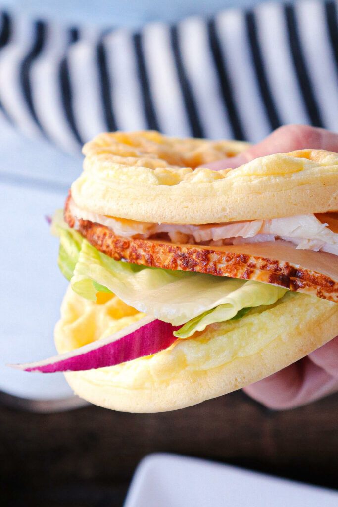 a person holding a sandwich with meat, cheese and lettuce in their hand