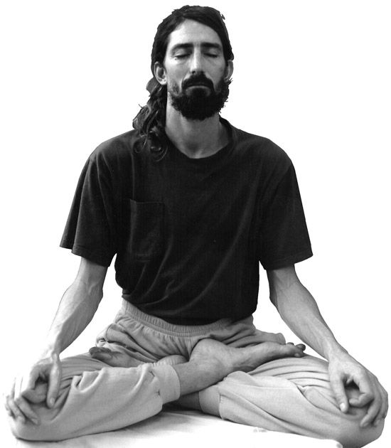 a man with long hair and beard sitting in the middle of a yoga pose while holding his hands together